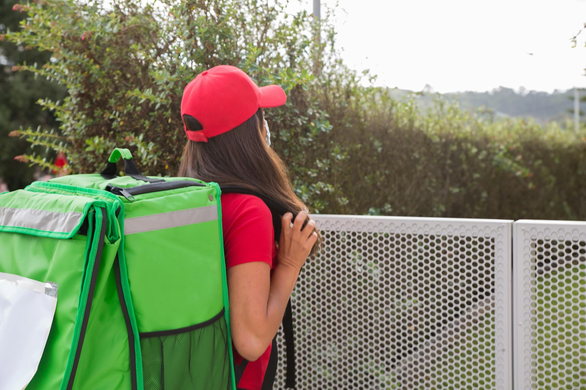 back view shot of a woman in red cap carrying insulated bag